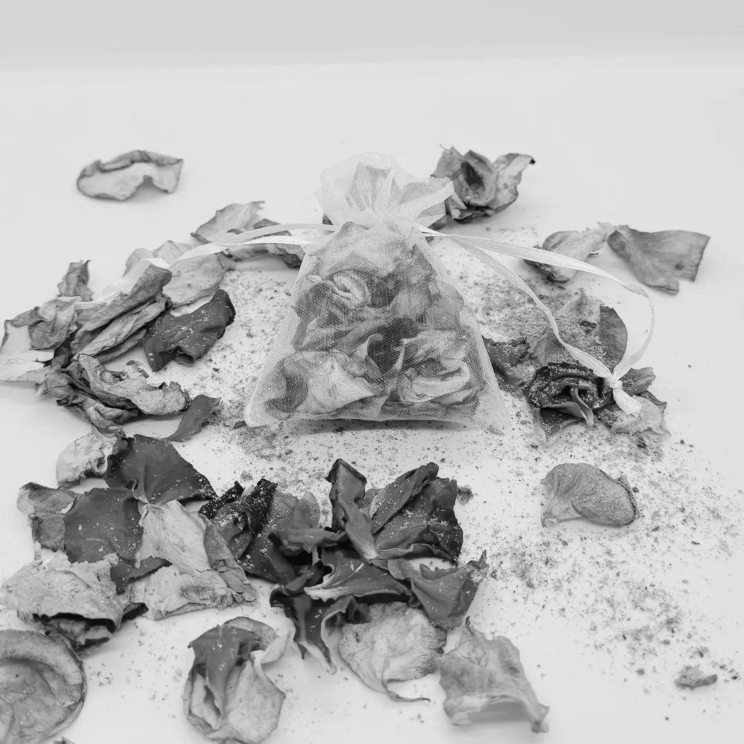 Costal de organza con pétalos de rosa secos, rodeado de más pétalos sueltos.