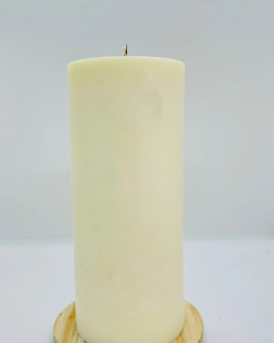 Cirio blanco de pilar, sin encender, sobre una base redonda de madera.