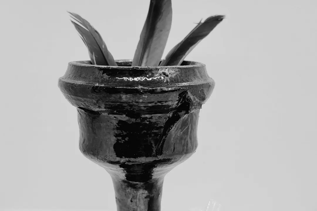 Copalera de barro negro vidriado en forma de cáliz, con un costal de hierba, un carbón y hierba molida esparcida.