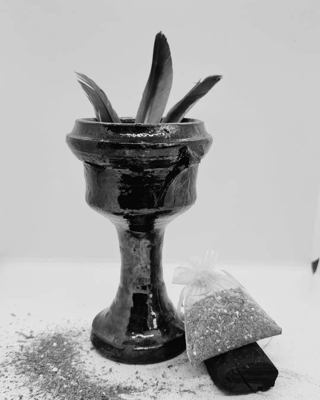 Copalera de barro negro vidriado en forma de cáliz, con un costal de hierba, un carbón y hierba molida esparcida.