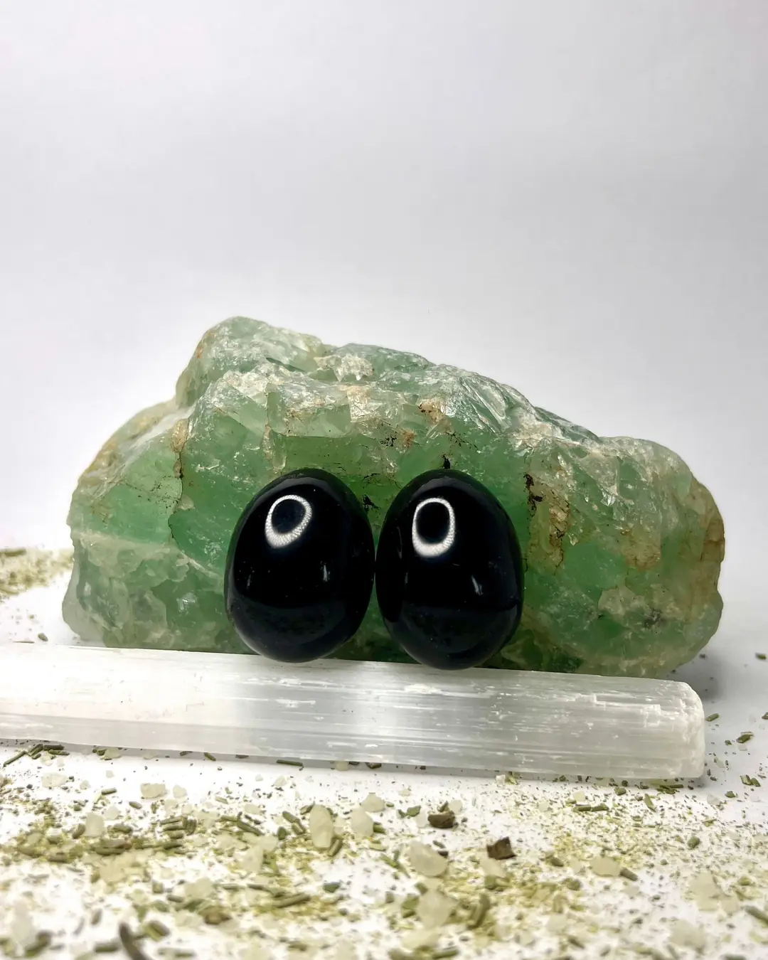 Dos huevos de obsidiana negra pulida frente a un trozo de fluorita verde y una barra de selenita.