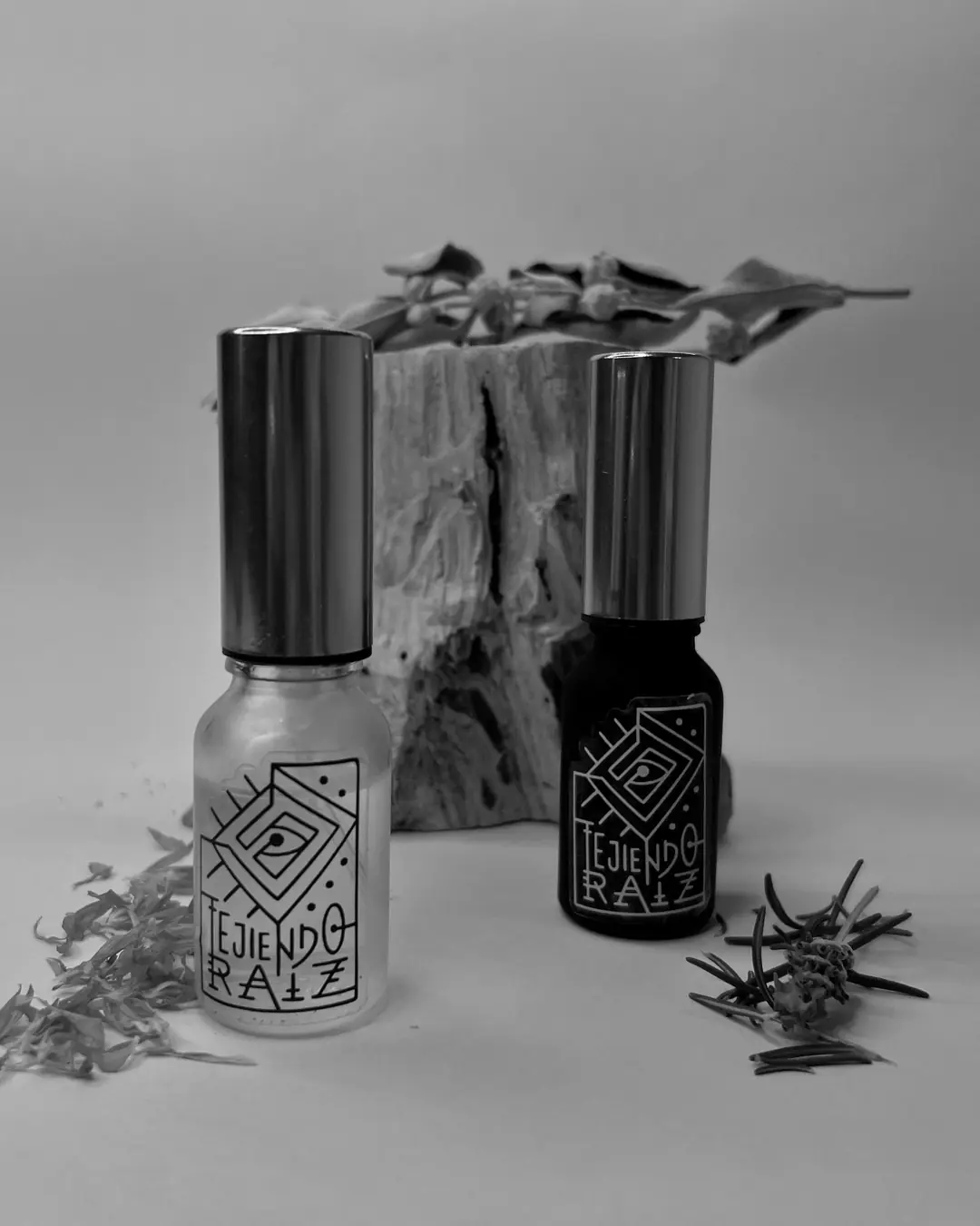 Dos frascos con atomizador junto a un tronco de palo santo, pétalos de caléndula y una rama de romero.