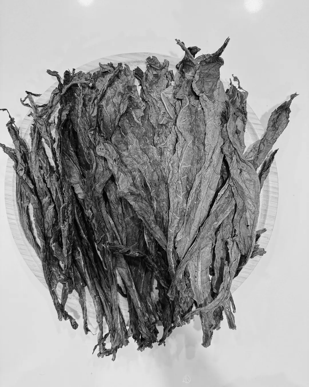 Hojas de tabaco secas, apiladas sobre un plato de madera, vistas desde arriba.